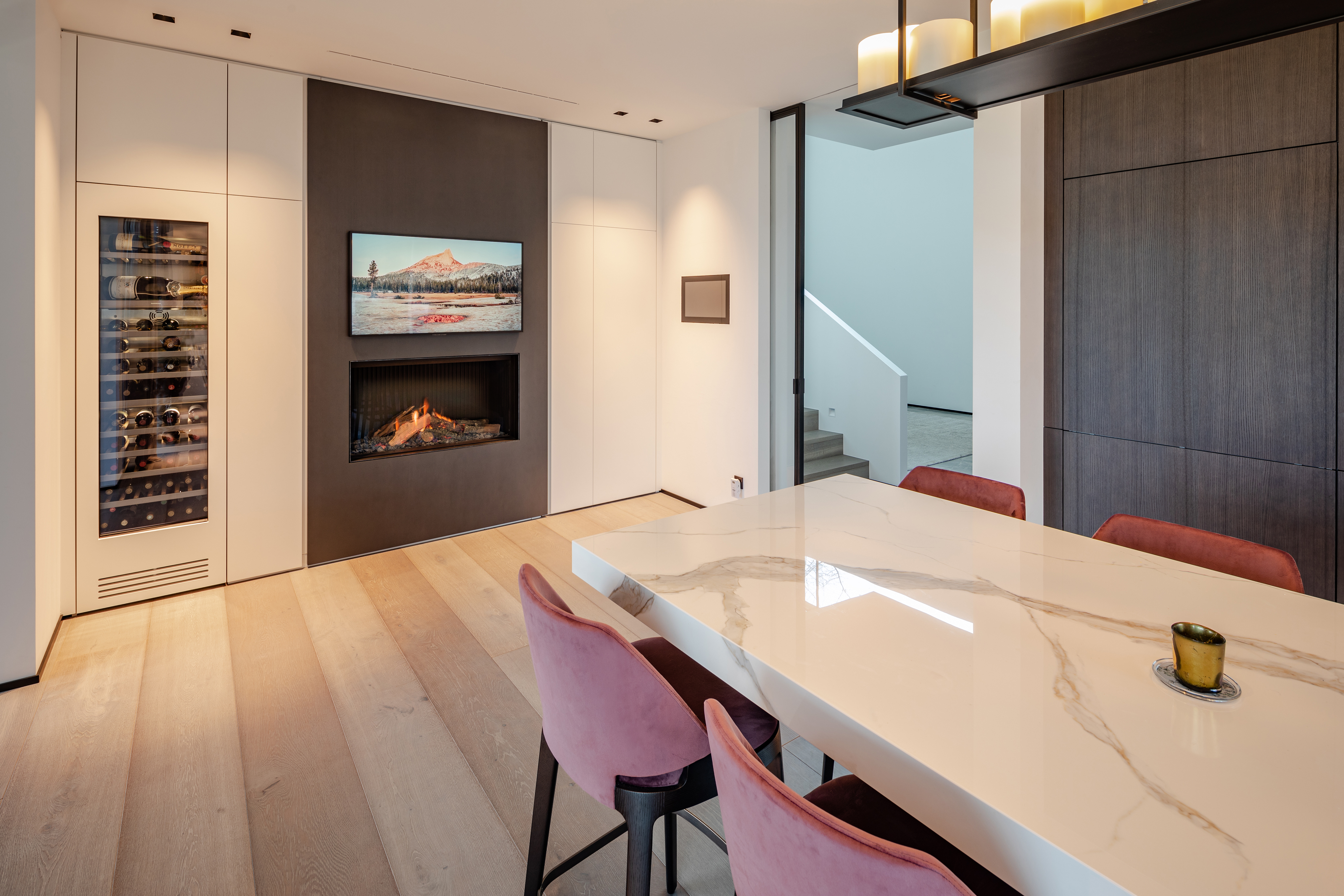 Modernes Esszimmer mit Kamin, Marmor-Esstisch, rosa Stühlen und integriertem Weinkühlschrank in stilvollem Ambiente.