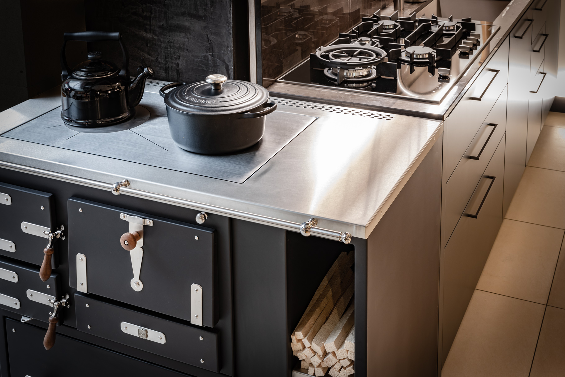 Moderne Küche mit Gasherd, Gusseisentopf, Wasserkessel und Holzherd mit integriertem Holzlager.