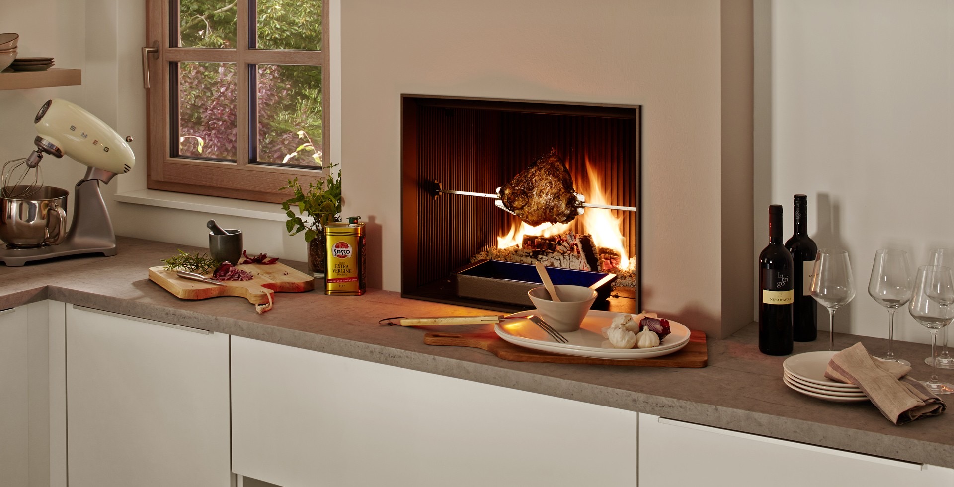 Küche mit offenem Drehspieß-Kamin, auf dem Fleisch grillt, umgeben von Wein, Zutaten und stilvoller Einrichtung.