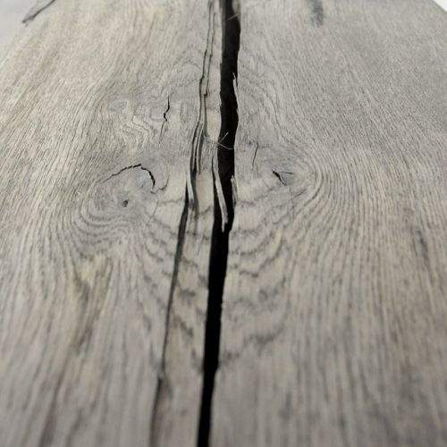 Nahaufnahme einer gealterten Holzoberfläche mit tiefer Rissbildung und sichtbarer Maserung in graubraunem Farbton.