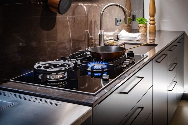 Gasherd mit blauer Flamme in moderner Küche, Topf auf dem Kochfeld, daneben Spüle, Gewürze und Küchenutensilien.