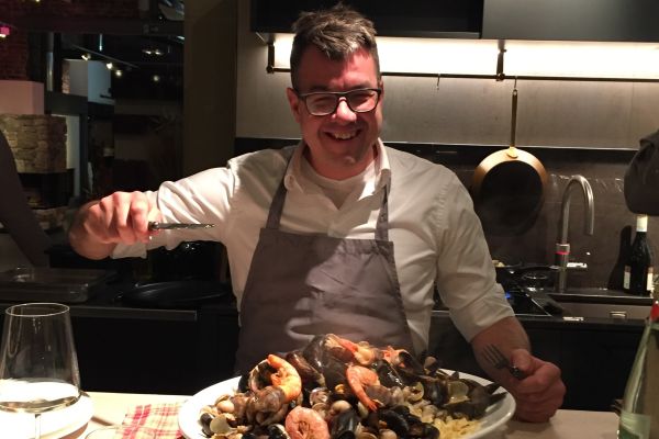 Koch in Schürze serviert fröhlich ein großes Meeresfrüchte-Gericht auf Risotto in einer modernen Showküche.